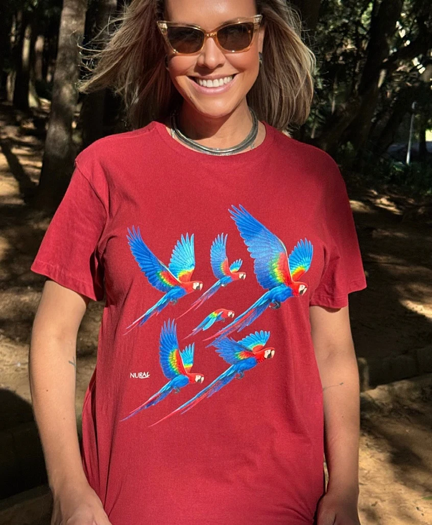 Thais usando uma camiseta Nura vermelha com estampa de araras, em ambiente natural